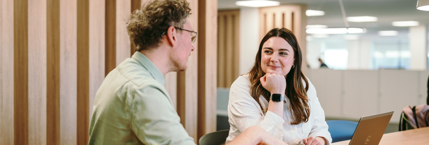 Two people sat at a desk talking