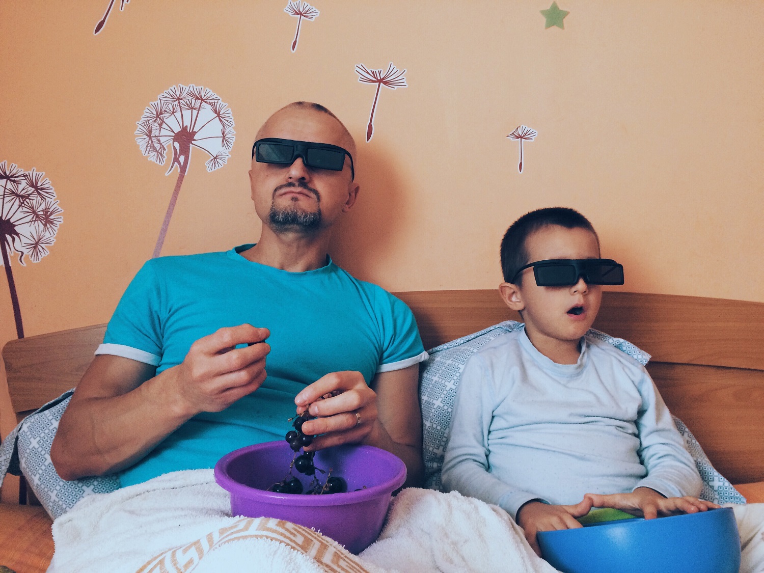 A dad and son sat with bowls of food and 3D glasses watching a film