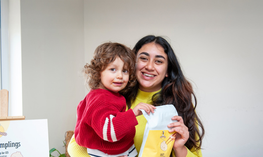 A mother and her child stand together holding a white bag of food