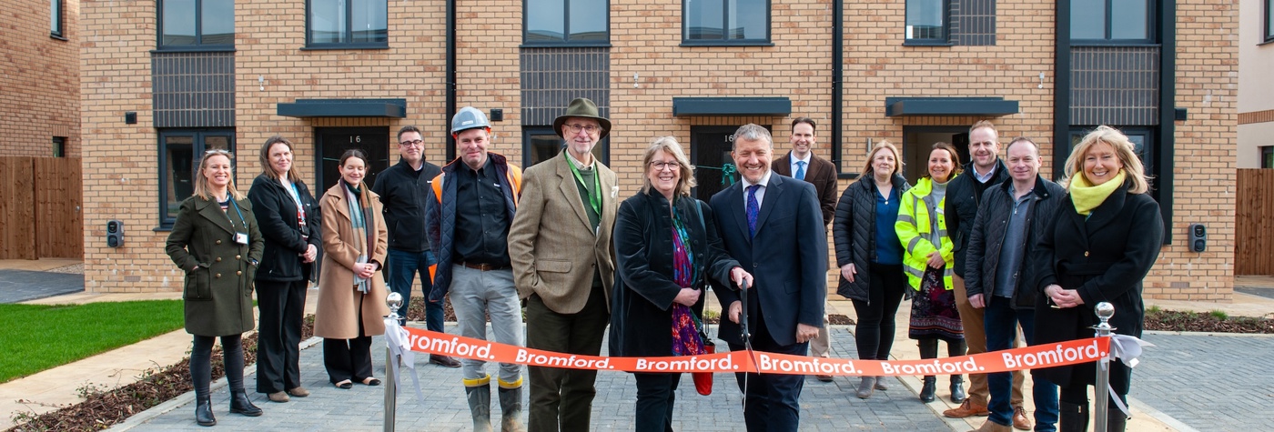 People standing in front of new homes and cutting an opening banner