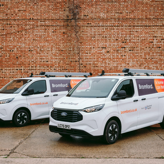 Two Bromford vans parked on an angle next to each other in front of a red brick wall.