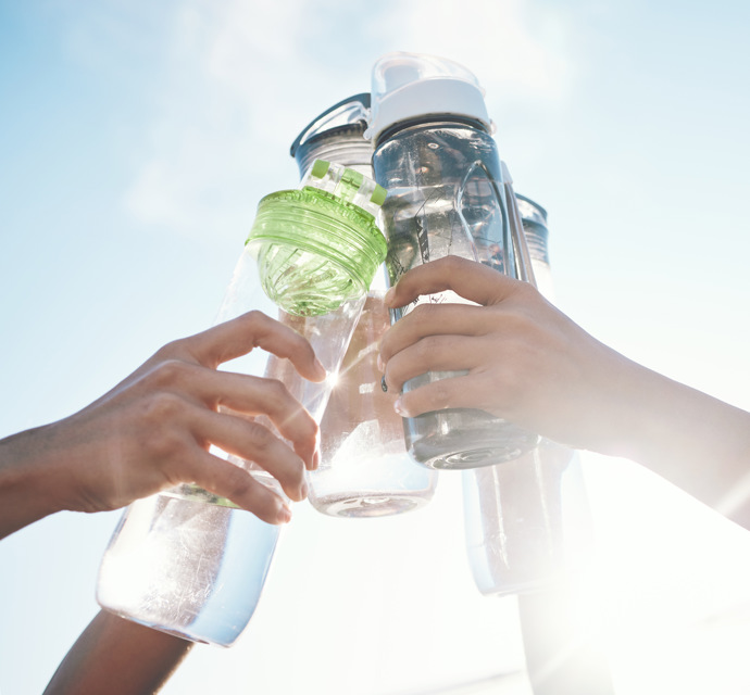 Four hands toasting four water bottles against a sunny sky