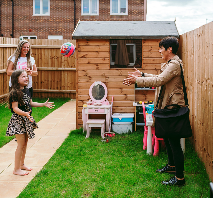 a bromford neighbourhood coach having fun throwing a ball a customer in the garden