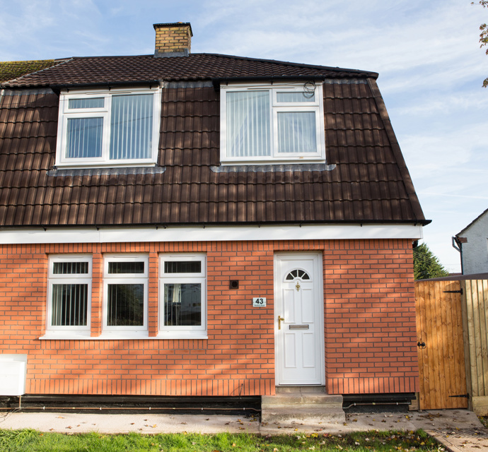 Exterior of a two-story semi-detached house with red brick ground floor, brown tiled mansard roof on the upper floor, white door, and white UPVC windows.