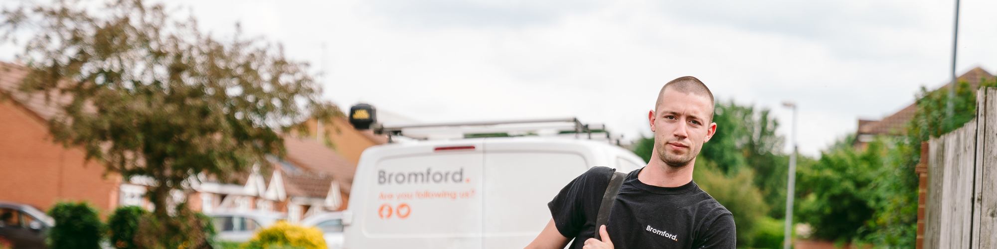A man walks in front of a parked Bromford van carrying a tool bag