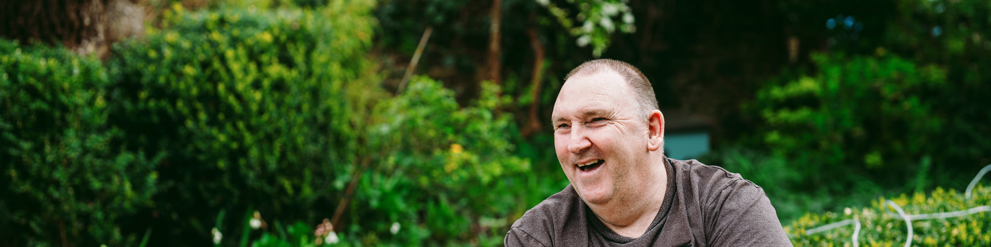A man sits outside with a t-shirt in a garden, the garden has spring flowers in the background