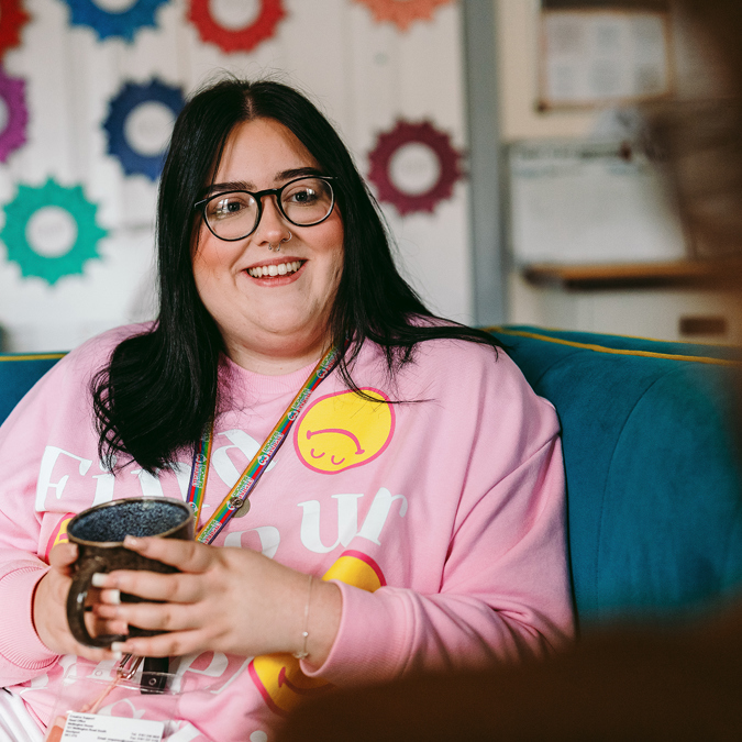 a bromford neighbourhood coach sat on a sofa with a warm drink