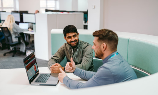 two Bromford colleagues talking in an office setting with an open laptop