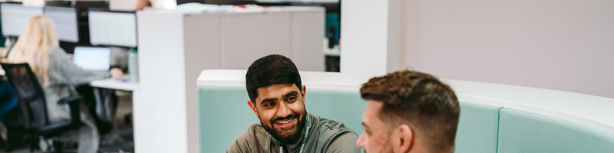 two Bromford colleagues talking in an office setting with an open laptop