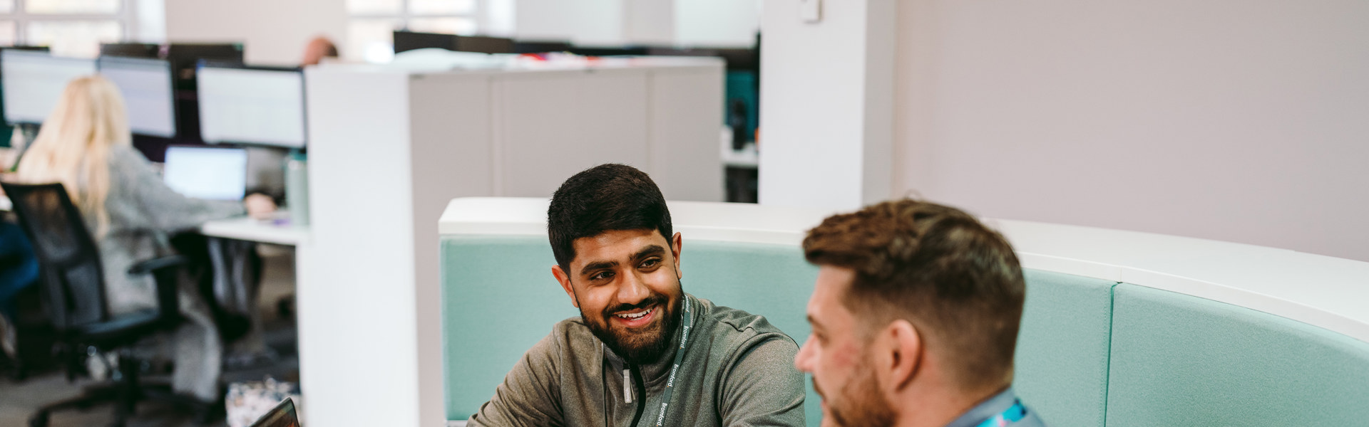 two Bromford colleagues talking in an office setting with an open laptop