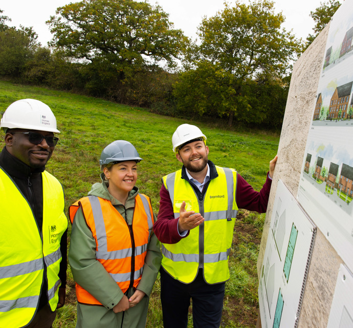 Two men and a woman in hi-vis jackets and hard hats look at plans for new homes at Hambrook