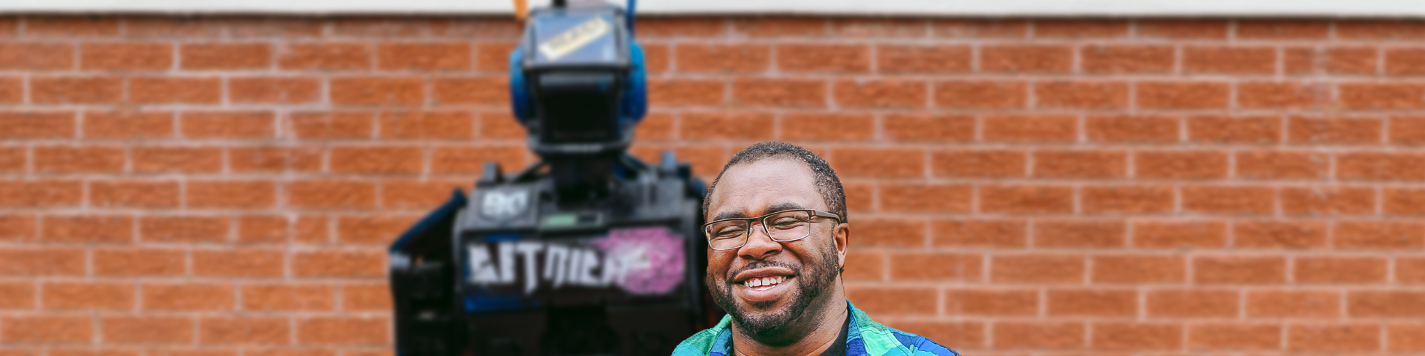 A man stands with arms crossed in front of a robot model