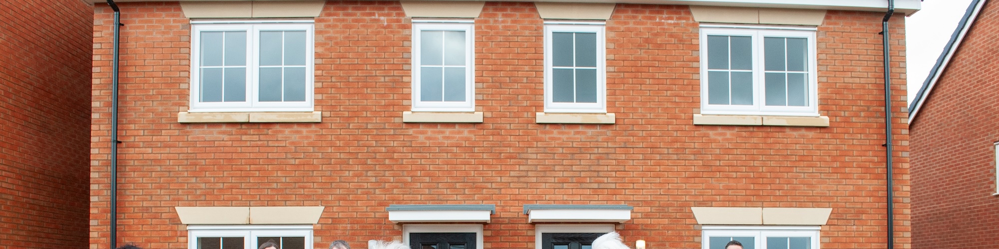 People standing in front of new homes and cutting a opening ribbon 