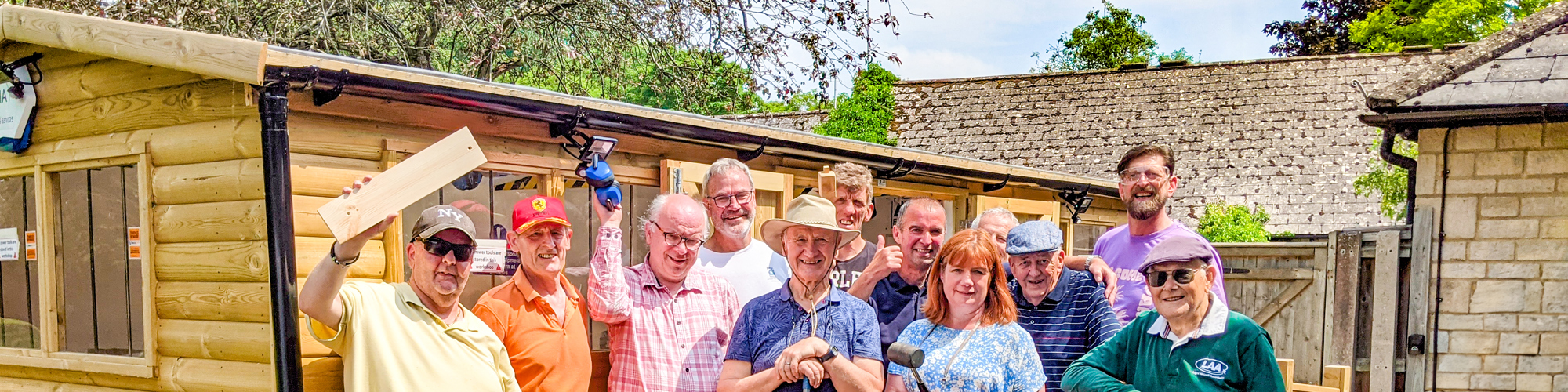 A group of 12 people stand in front of a shed