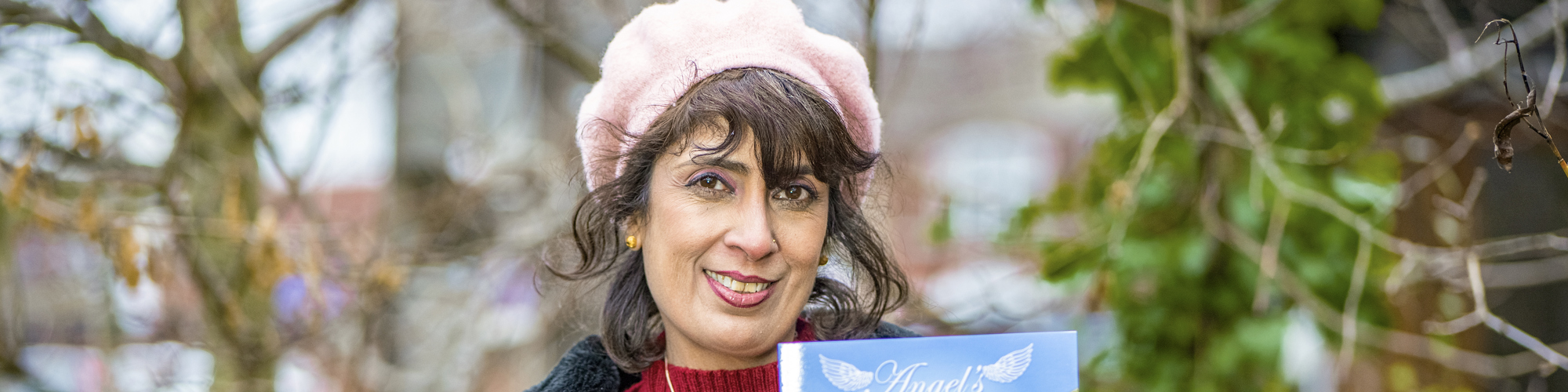 Gina stands outside holding a copy of her book