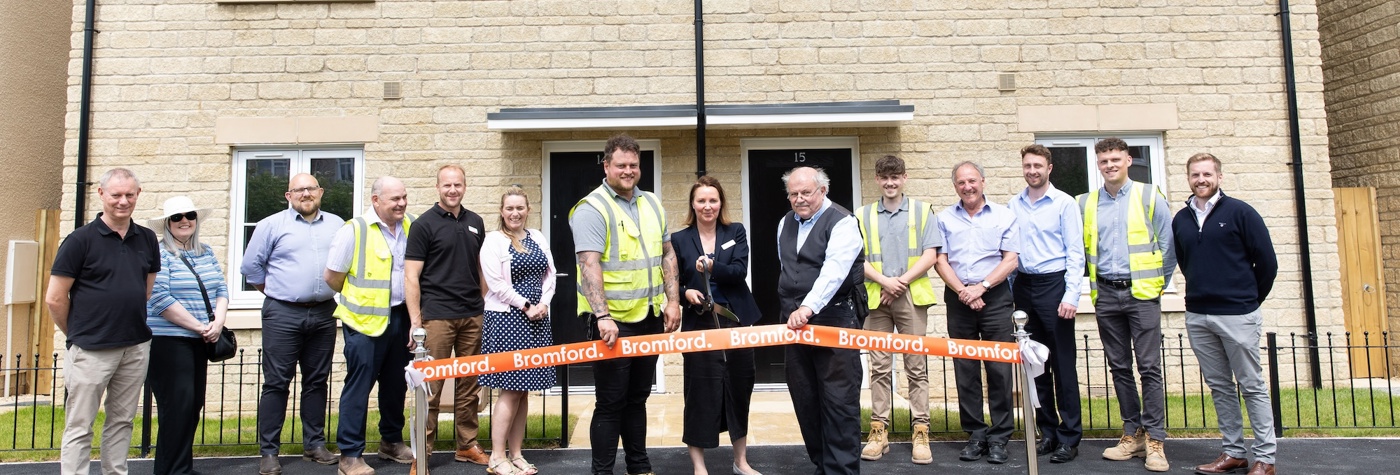 People standing in front of homes and cutting an opening banner