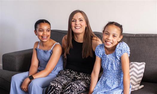 A woman sits with her two daughters on a sofa