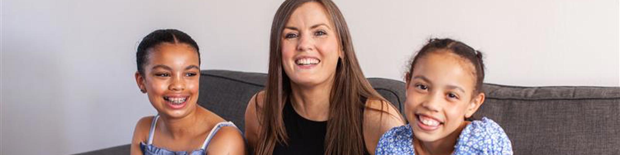 A woman sits with her two daughters on a sofa