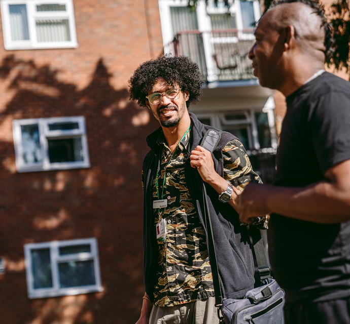A bromford neighbourhood coach talking to a customer in a communal area in front of some flats